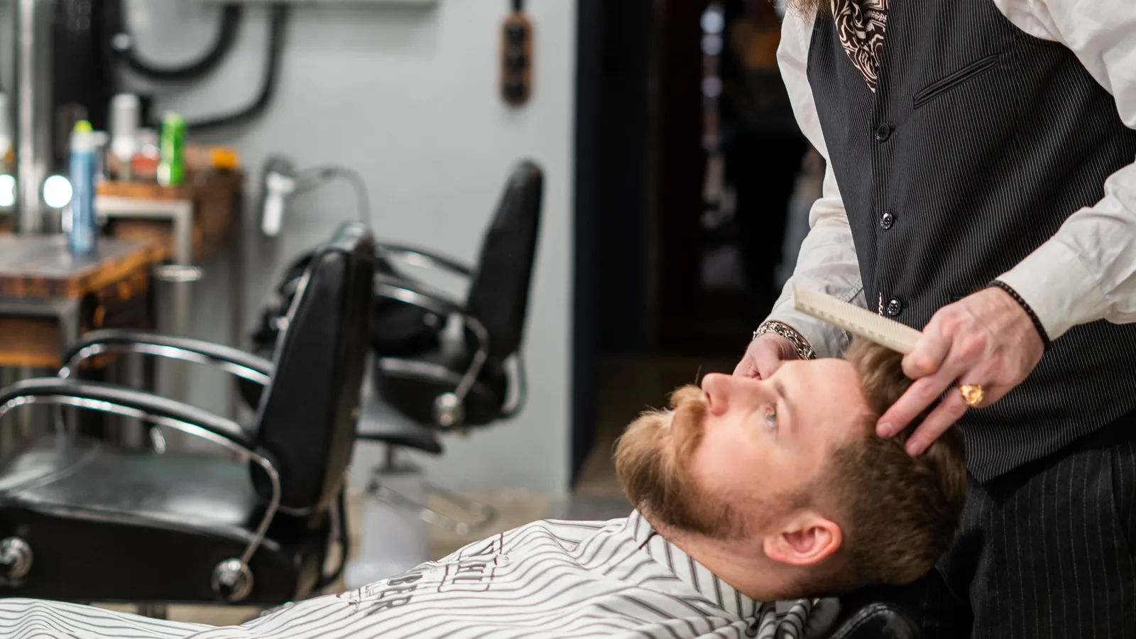 Barber combing a customer's red beard in a barbershop chair