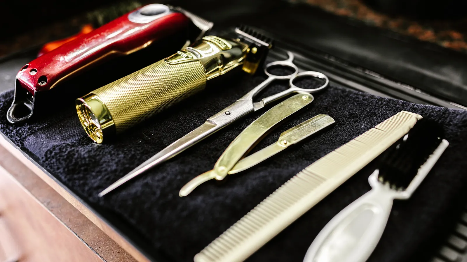 Barber's trimmers, scissors, razor and combs laid out on a black towel
