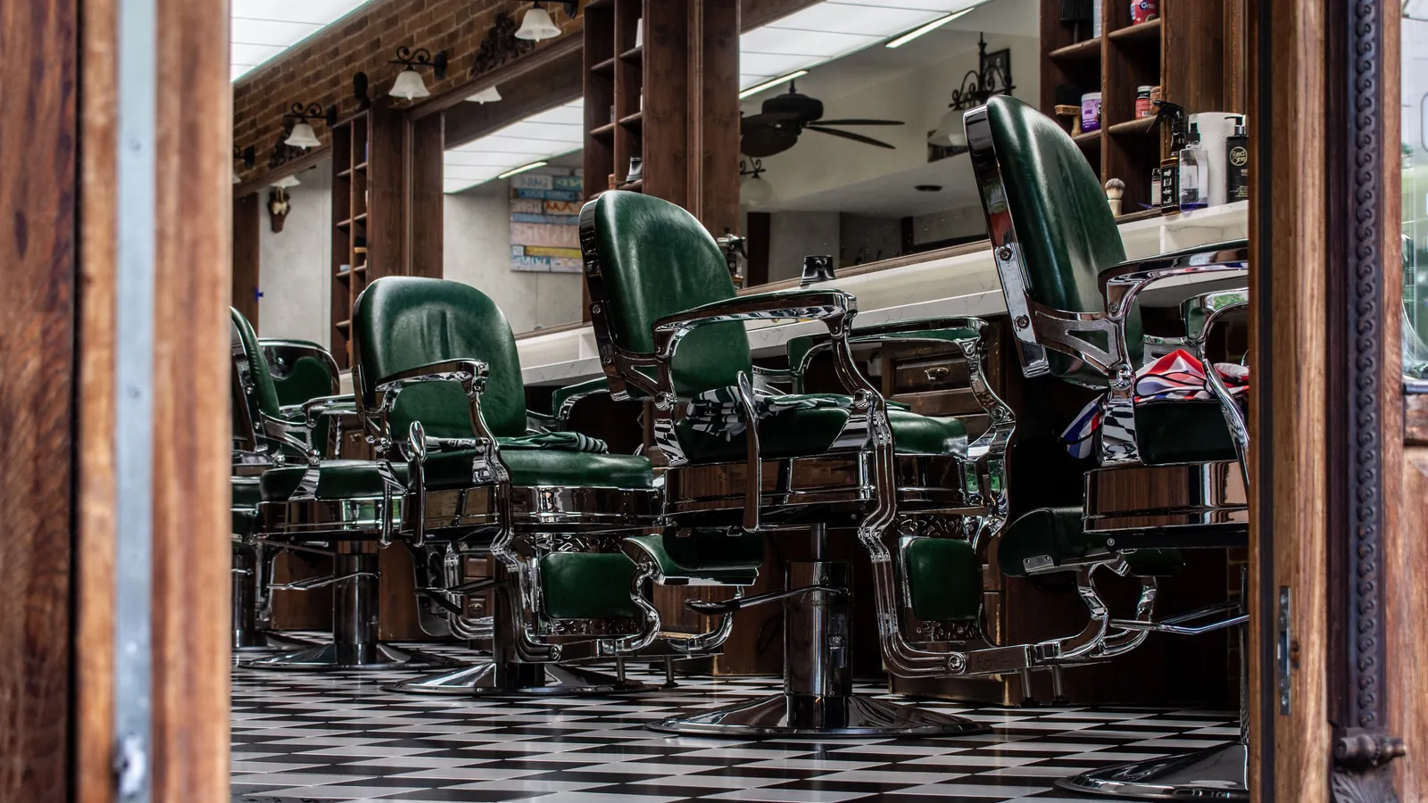 Row of green leather barber chairs on a black and white chequered floor in a traditional barber shop
