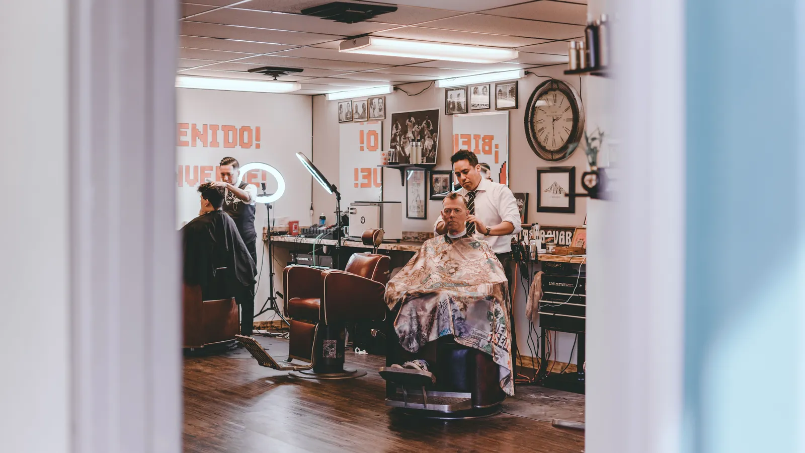 Two barbers cutting men's hair in a traditional barbershop with leather chairs and framed pictures