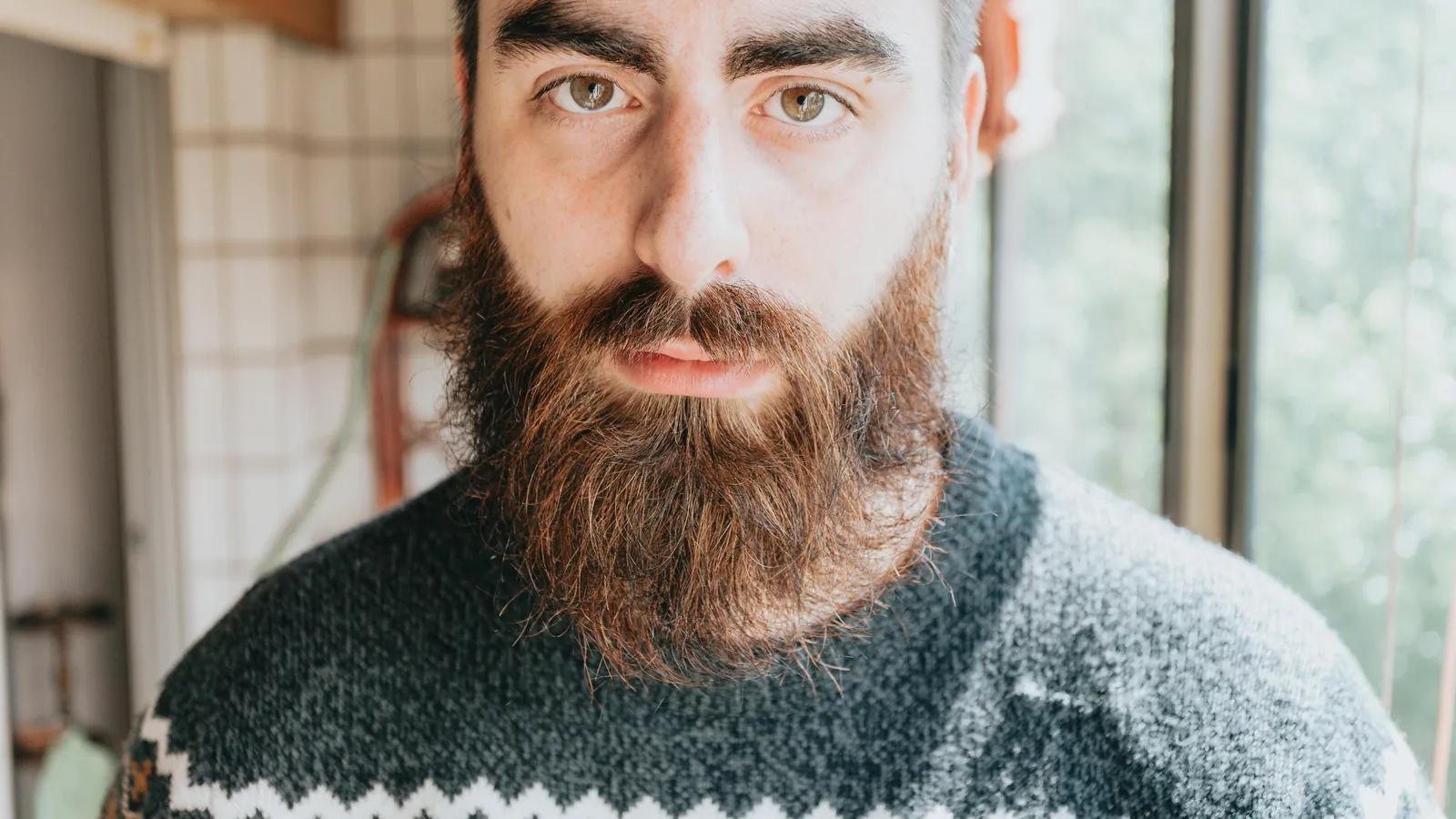 Man with a full, thick brown beard in a dark patterned jumper, facing the camera