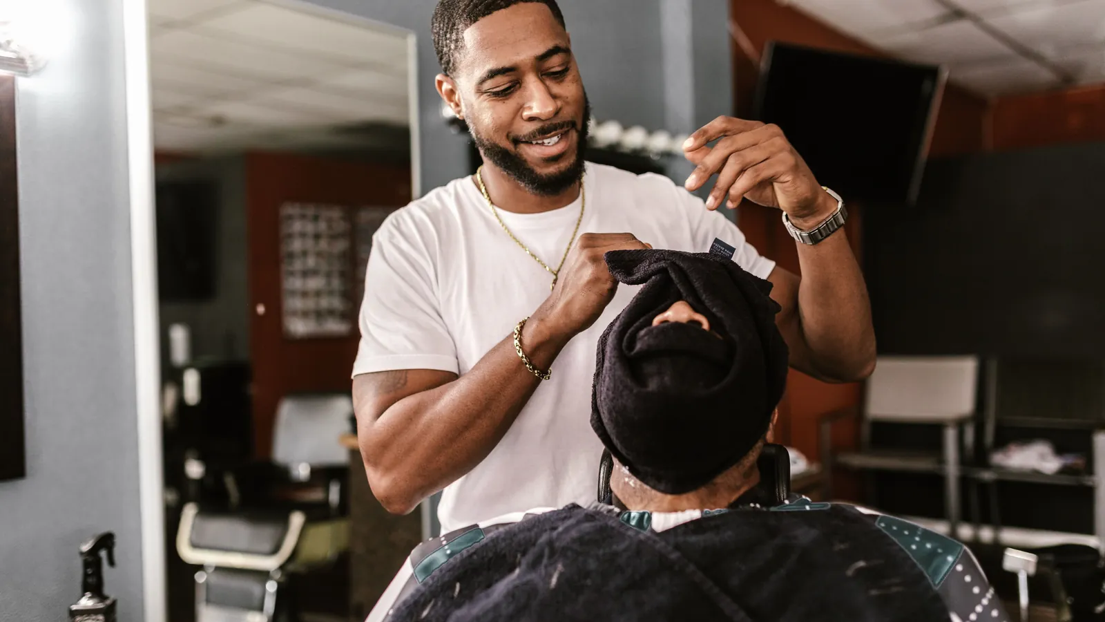 Barber wrapping a hot towel around a seated client's face in a barbershop