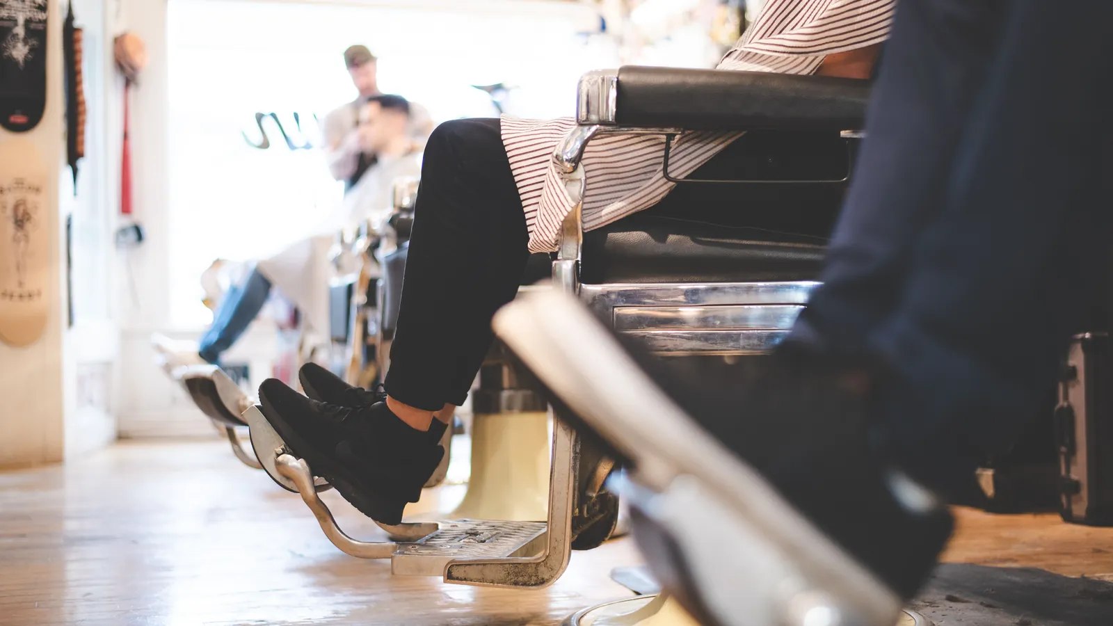 Customers seated in a row of barber chairs, with a haircut under way at the back of the shop