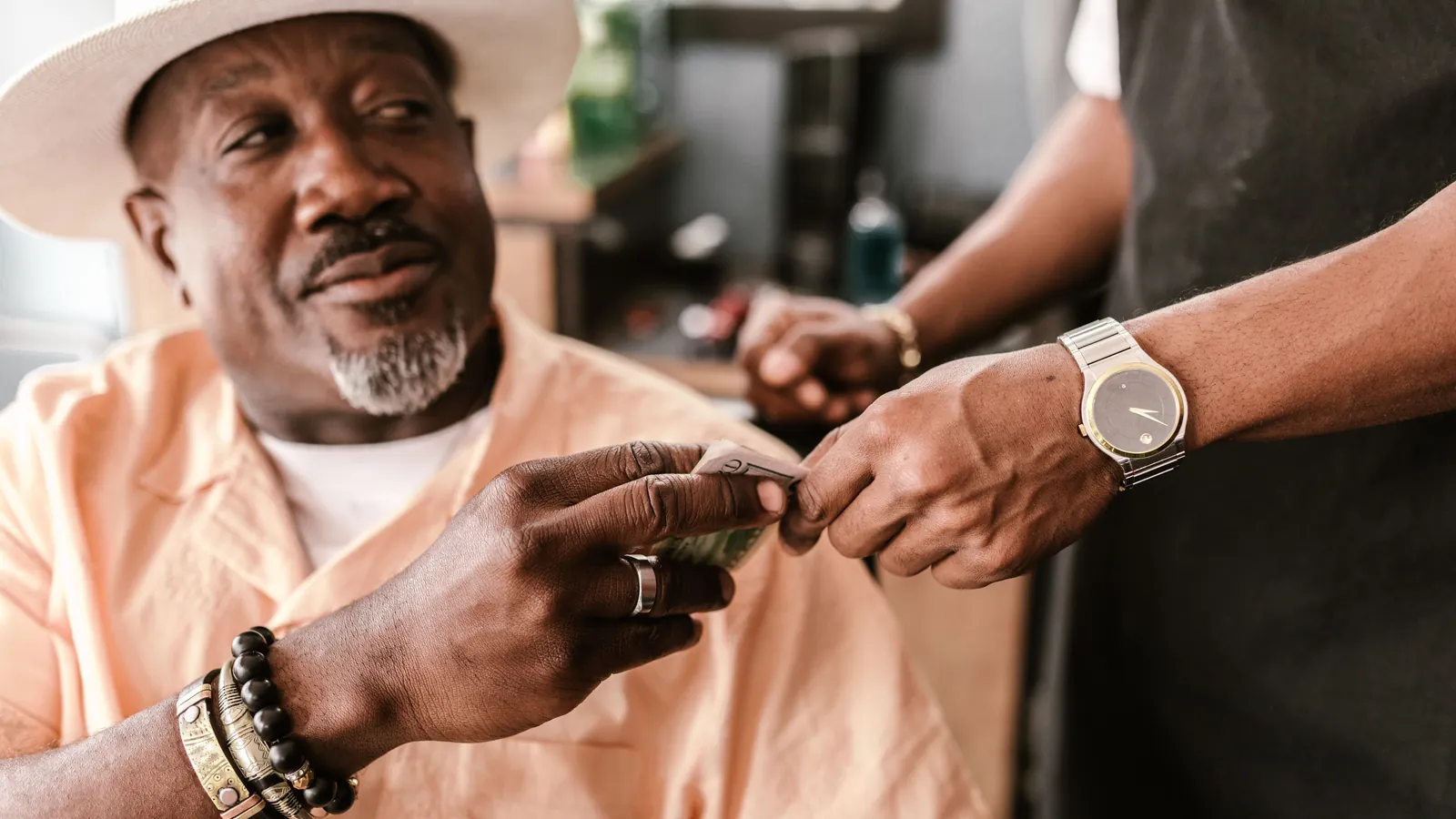 Customer in a barber's chair handing a folded banknote to his barber