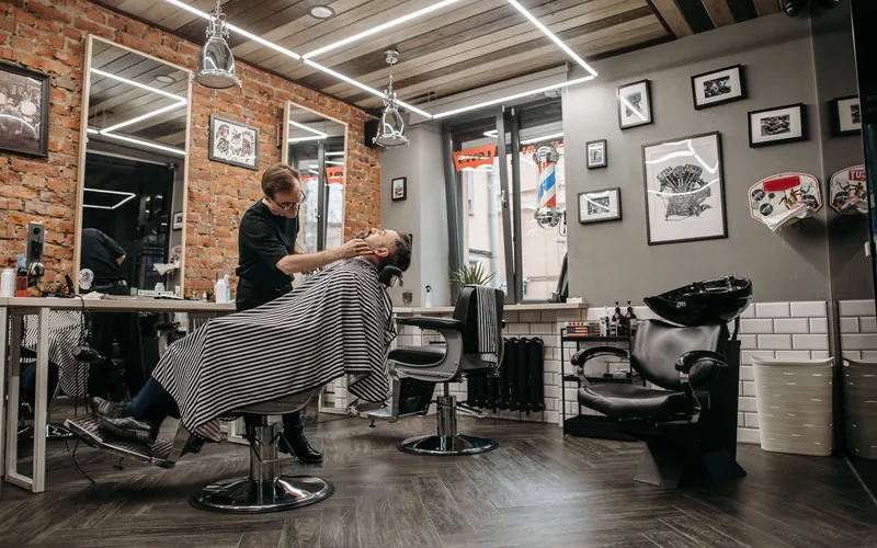 A barber cutting a client's hair in a barbershop with brick walls and framed pictures