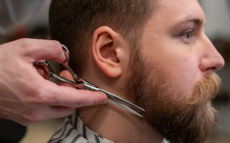 Side view of a barber trimming a bearded man's hair